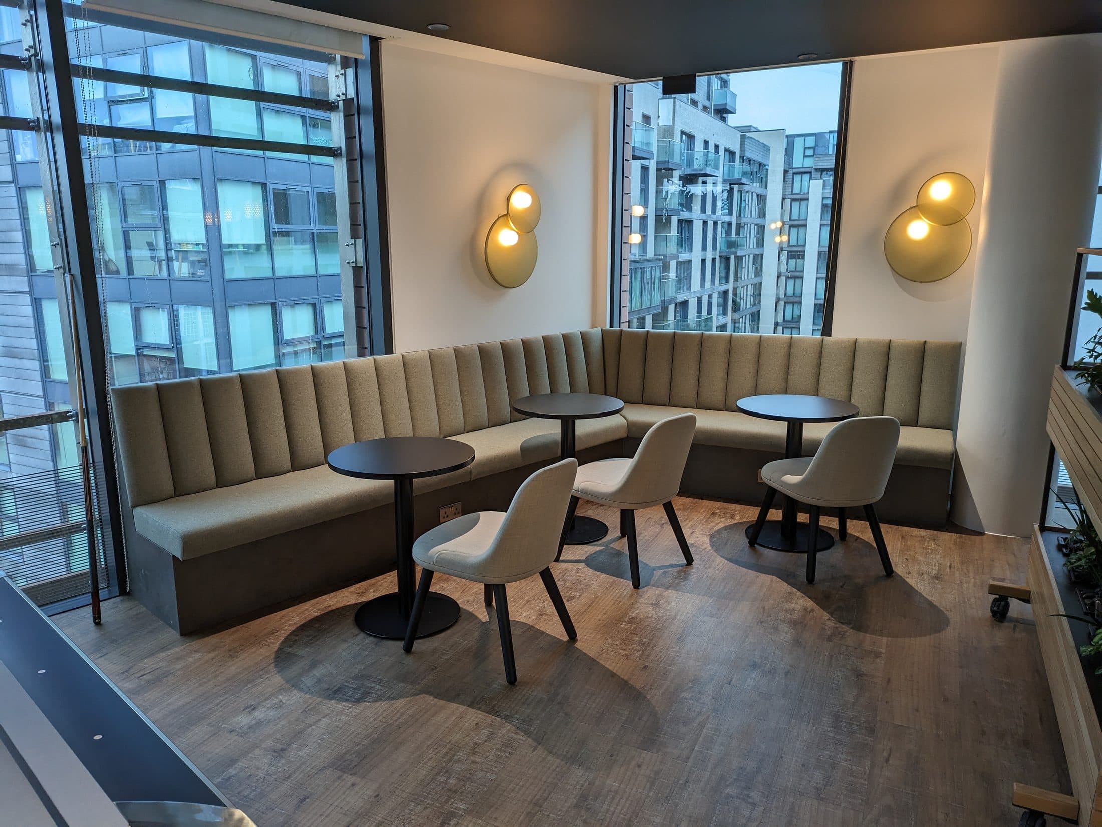 L-shaped sage fluted banquette in a glazed office corner with round tables